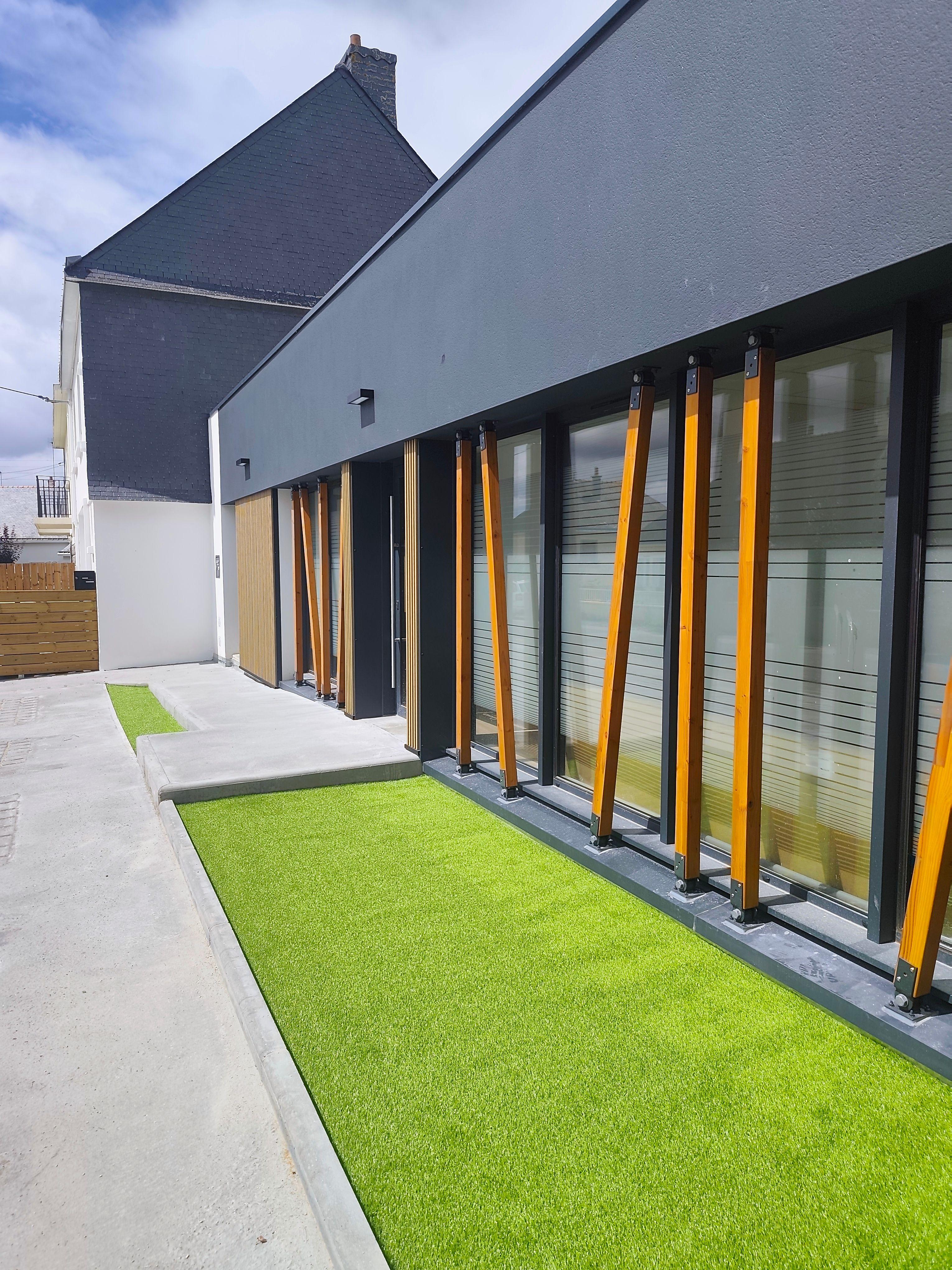 facade avec poteau bois et bardage imitation bois, faux gazon et rampe d'accès PMR, façade enduit anthracite et menuiseries alu ral 7016